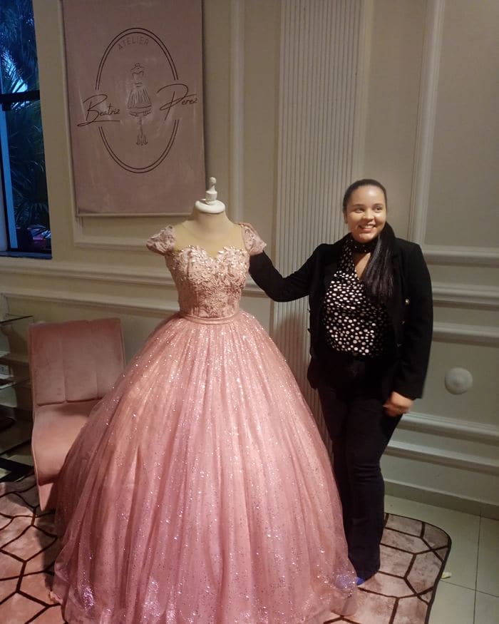 Beatriz Sosa ao lado de um vestido rosa no ateliê